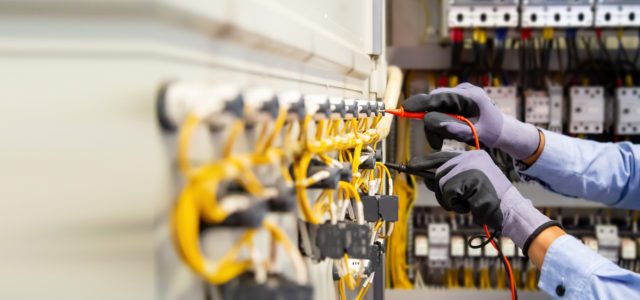 Electrical engineer using digital multi-meter measuring equipment to checking electric current voltage at circuit breaker and cable wiring system in main power distribution board.