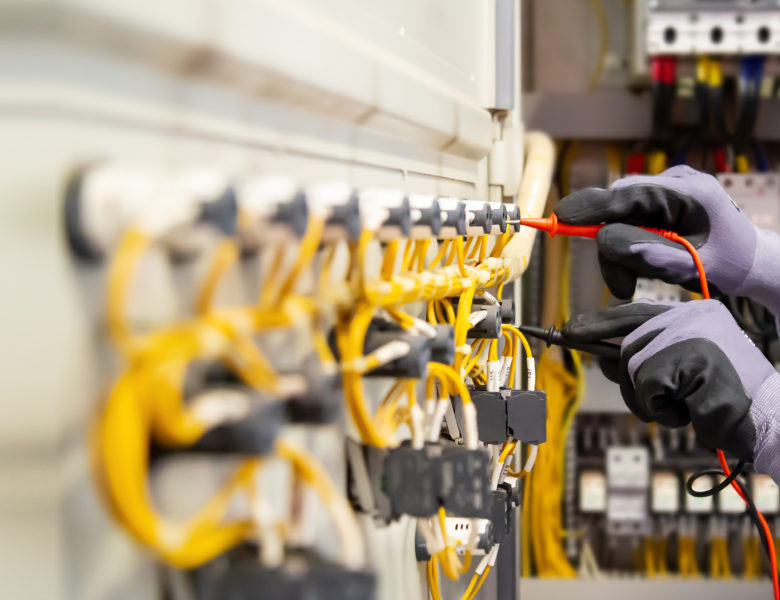 Electrical engineer using digital multi-meter measuring equipment to checking electric current voltage at circuit breaker and cable wiring system in main power distribution board.